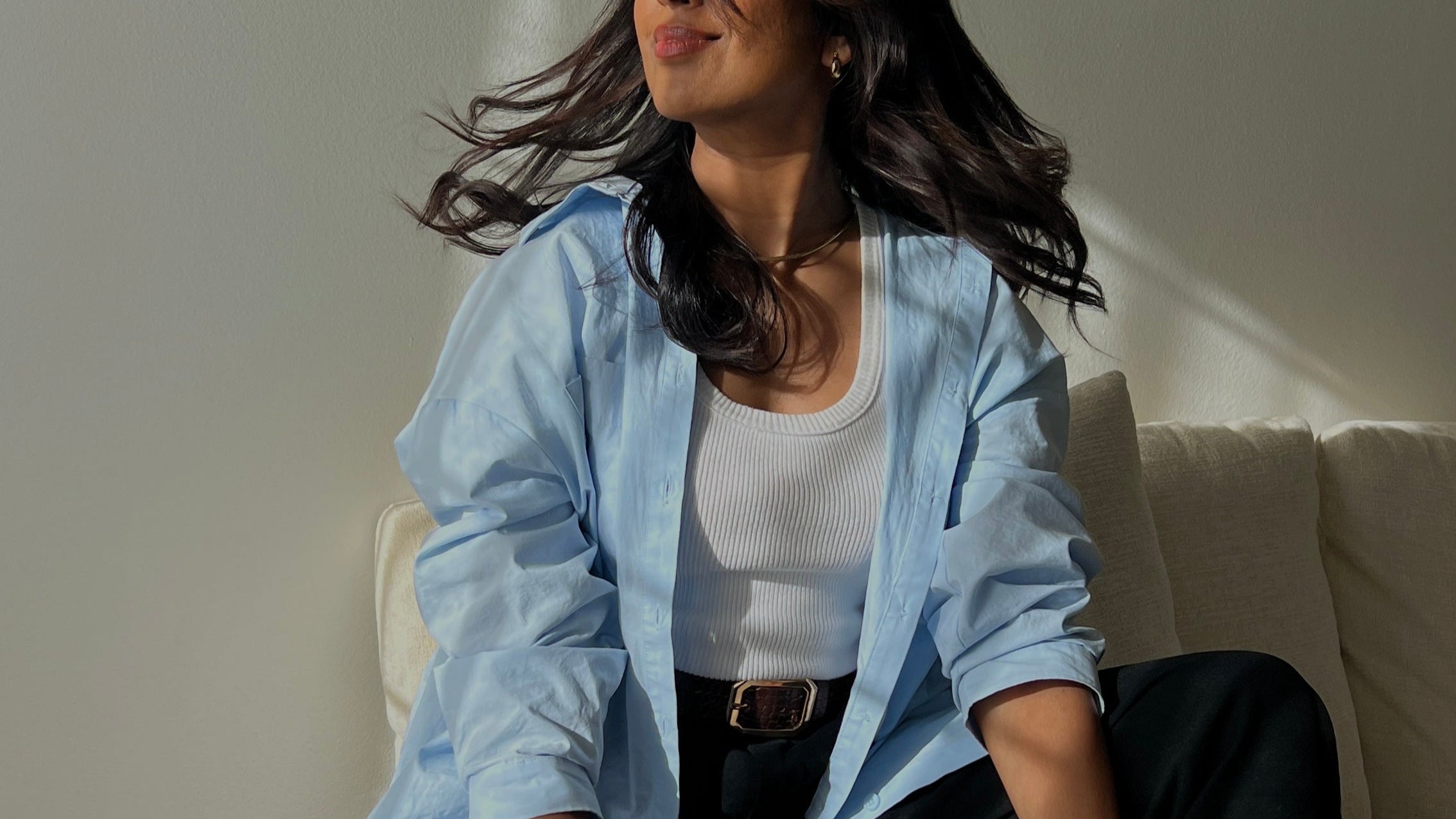 Woman sitting on a white couch wearing a light blue shirt and black pants.